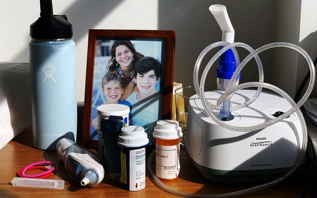 A photo of a framed family photograph, a nebulizer, a Hydro Flask, and bottles of pills on a desk