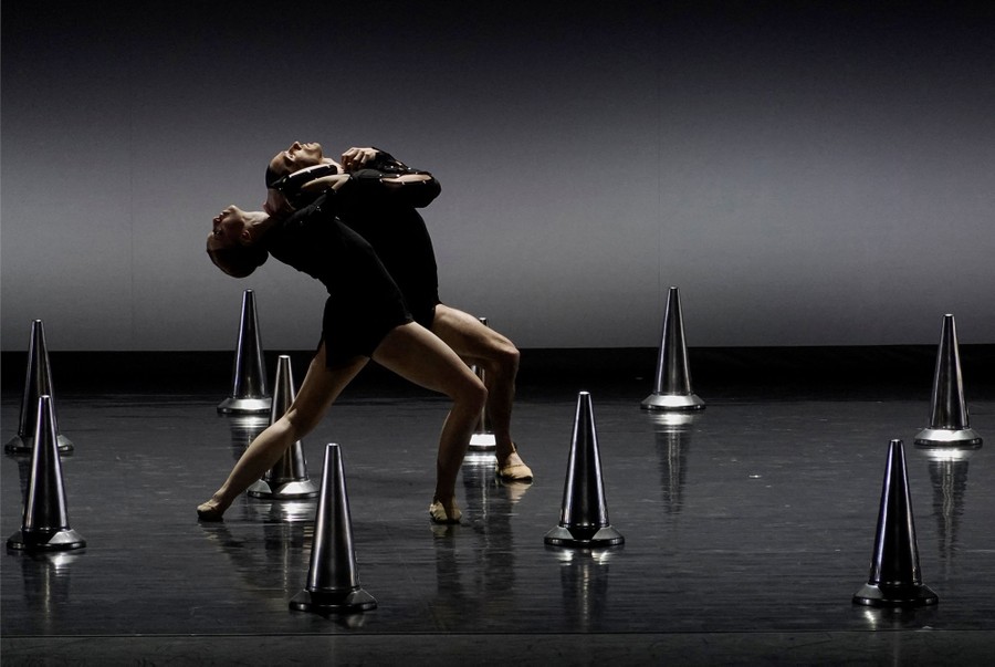 Two dancers perform on a stage among small pylons.
