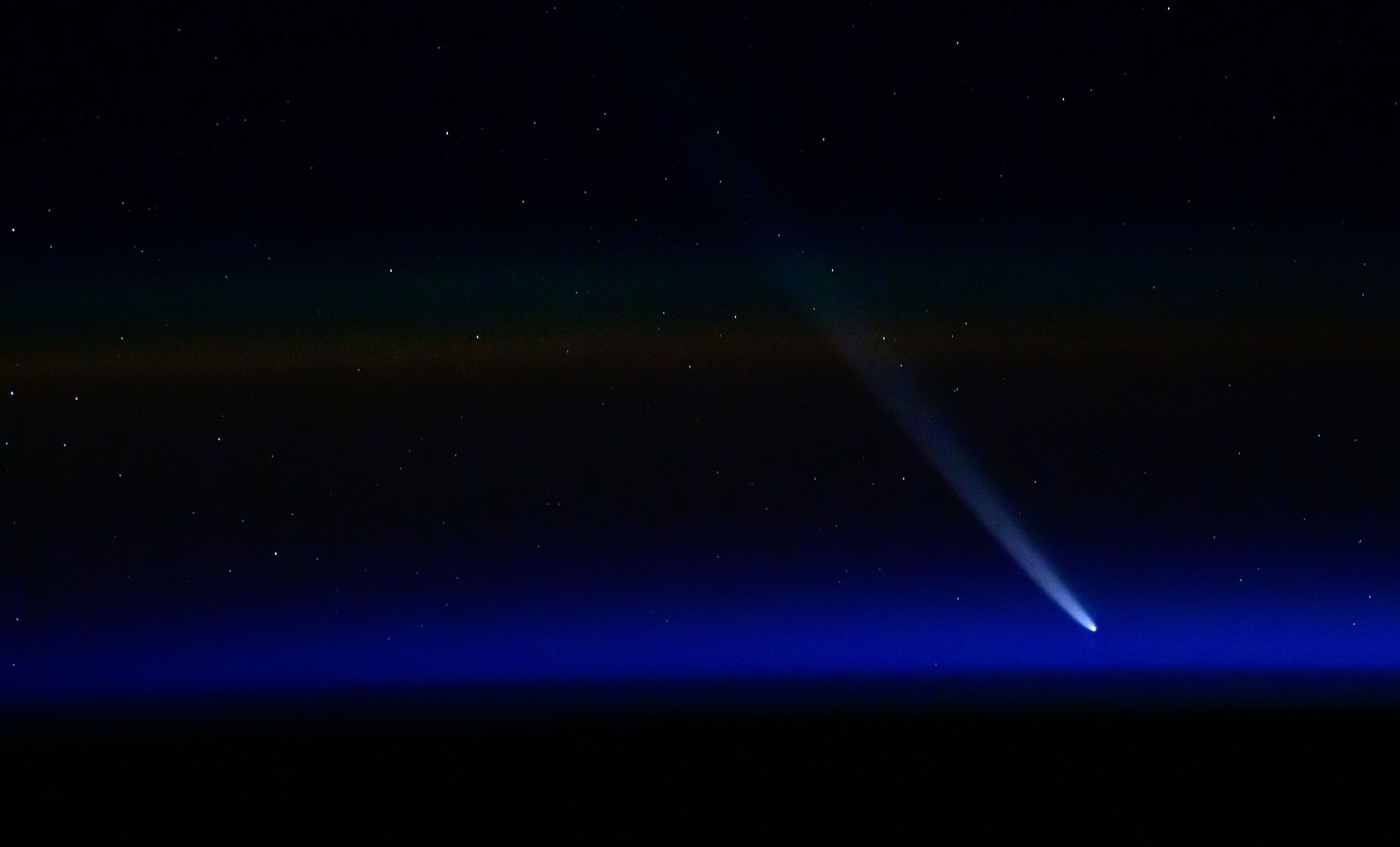 A distant comet, seen passing near blue light at the Earth's horizon.