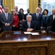 Donald Trump at his desk surrounded by people, including Mike Pence