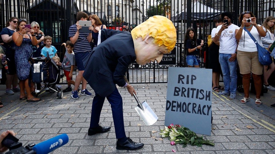 A man wearing a Boris Johnson mask stands outside Downing Street, pretending to dig a grave for "British Democracy."