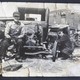 A black-and-white photo of a man sitting on an old-fashion car in the 1930s or 1940s