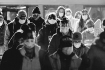 People stand together wearing masks and bundled in warm clothing.