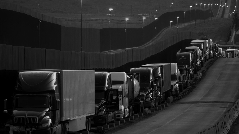 Black-and-white photo of a line of trucks near the Mexico-U.S. border