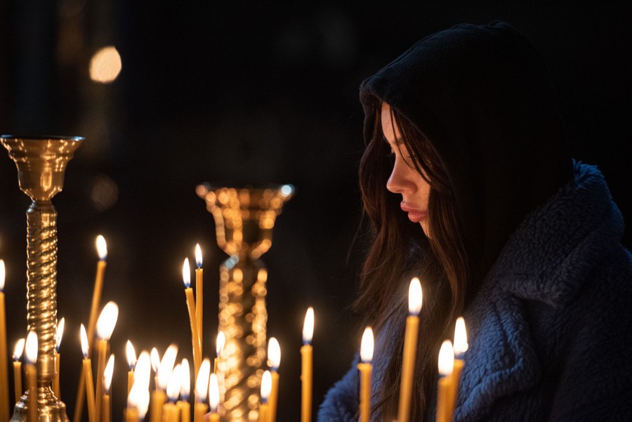 A woman standing in a cathedral in front of numerous lit candles.