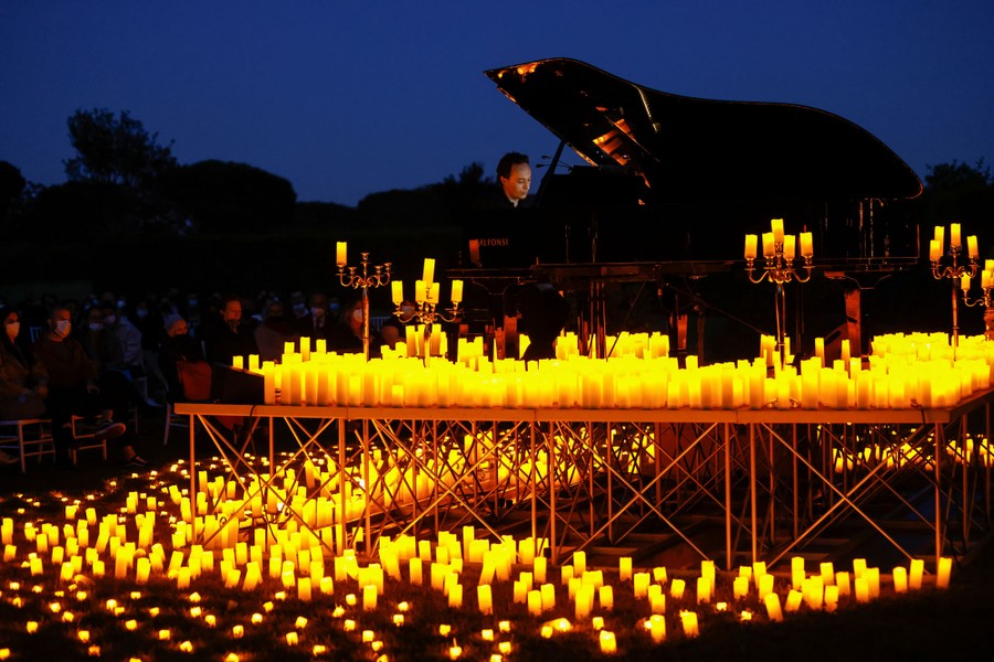 A pianist plays on an outdoor stage surrounded by hundreds of lit candles.