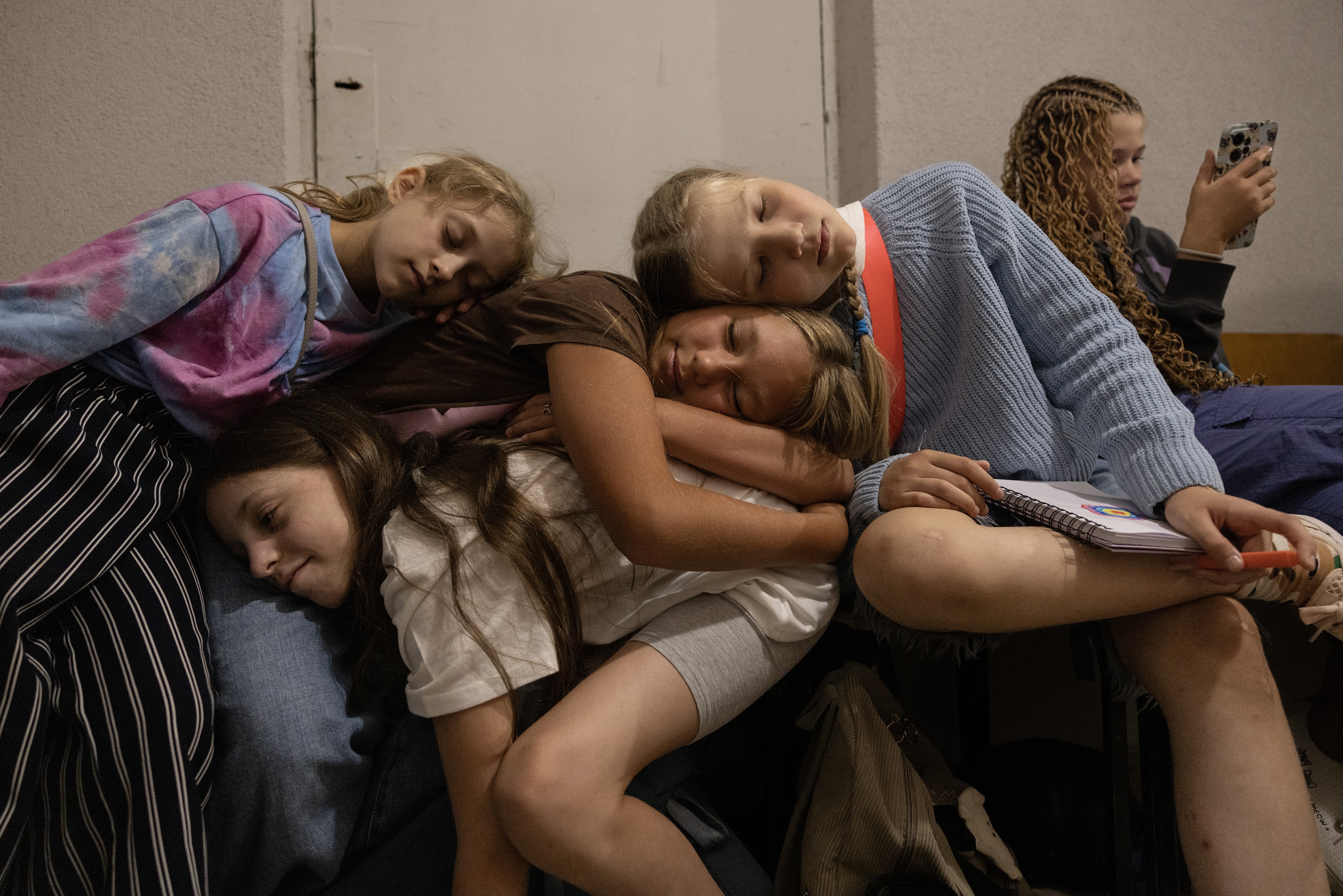 Several young students lean and lie on each other inside a shelter in Ukraine.