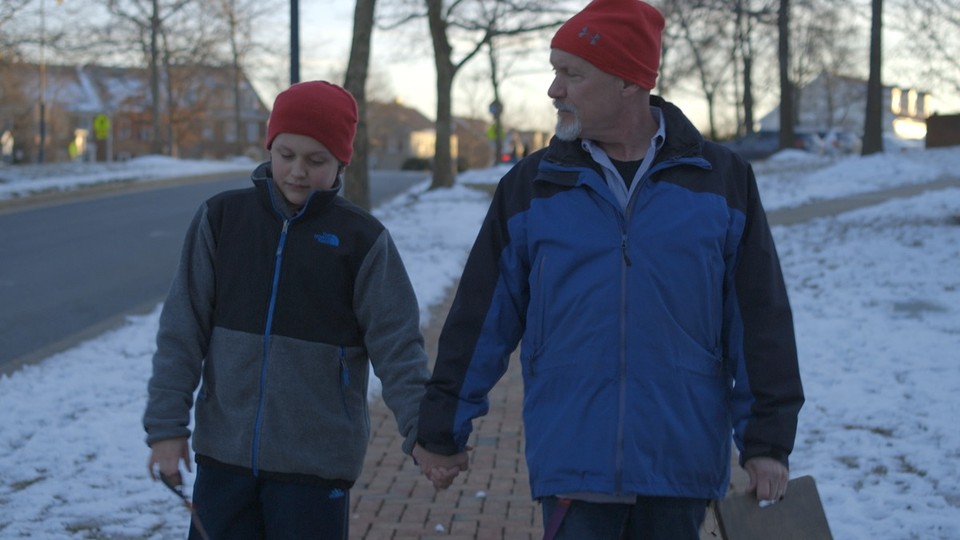 A boy and his father walk along a snowy street holding hands