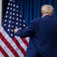 Trump with his back turned, in front of two American flags