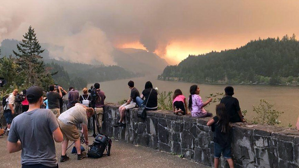 People watch a wildfire burning in a mountain range.