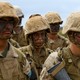 Photo of a female U.S. soldier surrounded by other soldiers in desert-camo uniforms with their faces painted, holding rifles