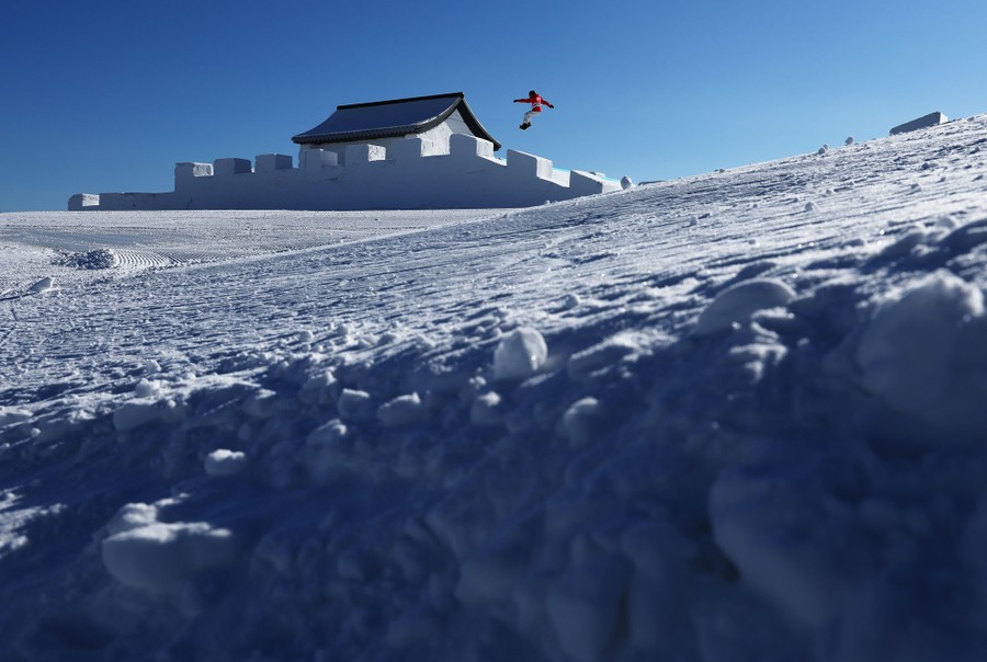 A snowboarder jumps off the roof of an obstacle on a ski slope.