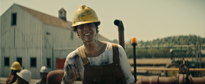Justin Bieber, covered in mud, wears a yellow hard hat and Dickie's overalls and grimaces toward the viewer.