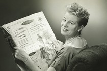 A black-and-white image of a woman reading a 1950s newspaper