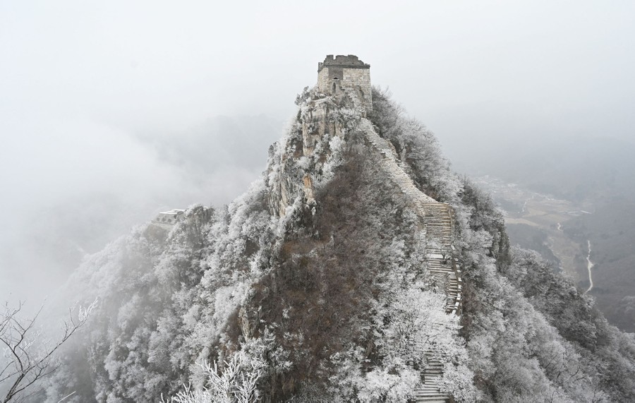 An aerial view of a steep snow-covered hill, topped by a watchtower and part of the Great Wall of China.