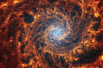 A tight view of a face-on spiral galaxy anchored by a central region that has a light-blue haze, surrounded by complex orange-colored spiral arms