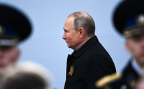 Putin, frowning, strides past men in military uniform.