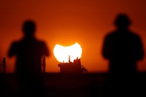 Two people look at a distant sunset, with part of the sun occluded by a partial eclipse.