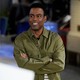 Comedian Chris Rock smiles and looks to the left, with his arms crossed.