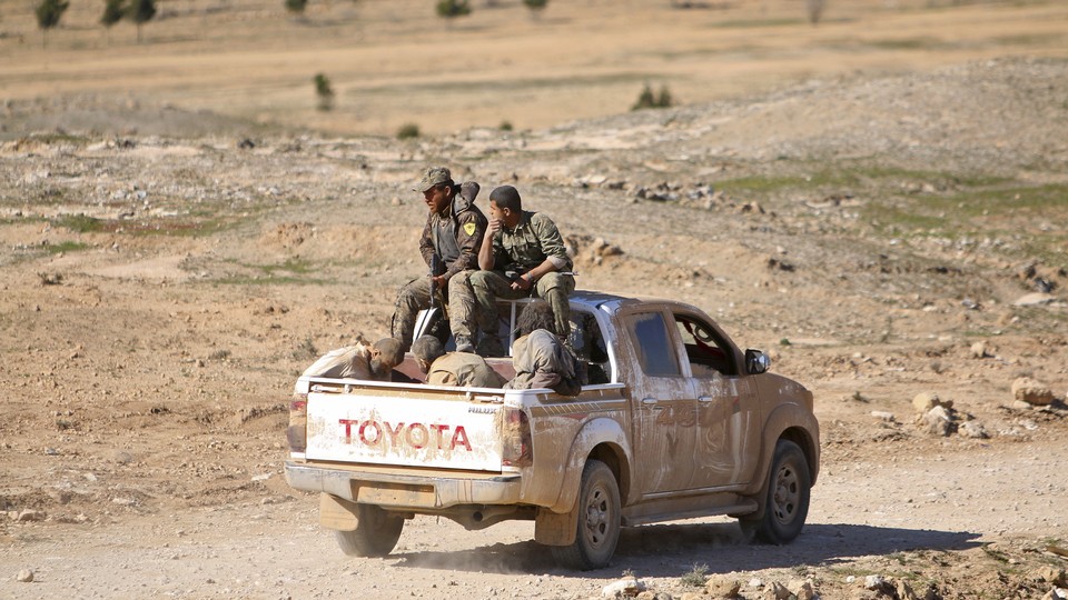 Fighters in the Syrian Democratic Forces ride a pickup truck with Islamic State fighters held as prisoners near al-Shadadi town, in the Hasaka countryside of Syria, on February 18, 2016.