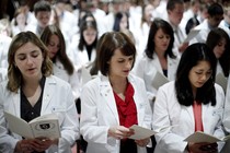 A group of students in white lab coats reads from pamphlets.