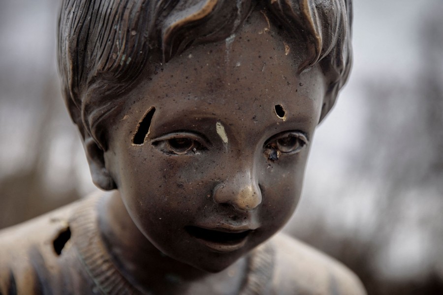 The face of a bronze statue of a child has several holes in it, made by flying shrapnel.