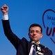Ekrem İmamoğlu speaks at a rally with a heart graphic in the background.