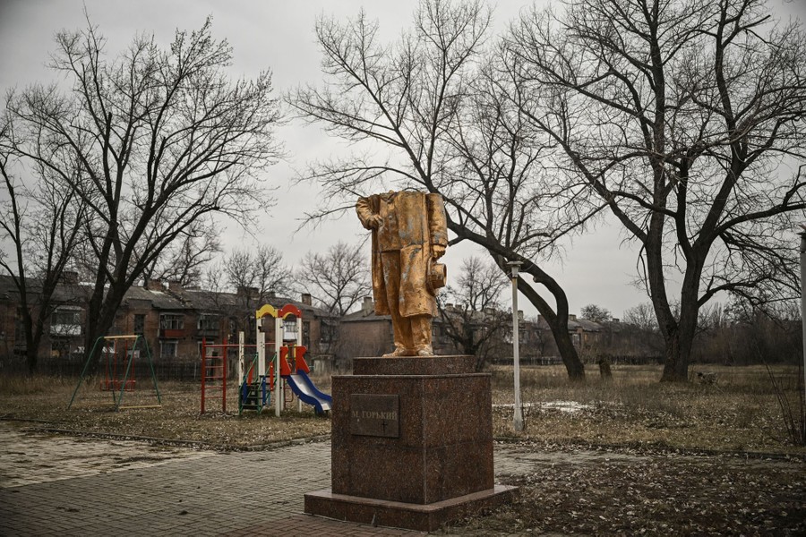 A statue stands in a park, missing its head and shoulders.