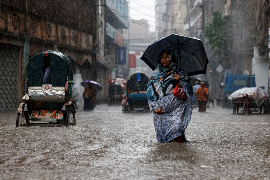 A woman holds an umbrella while walking along a flooded street.