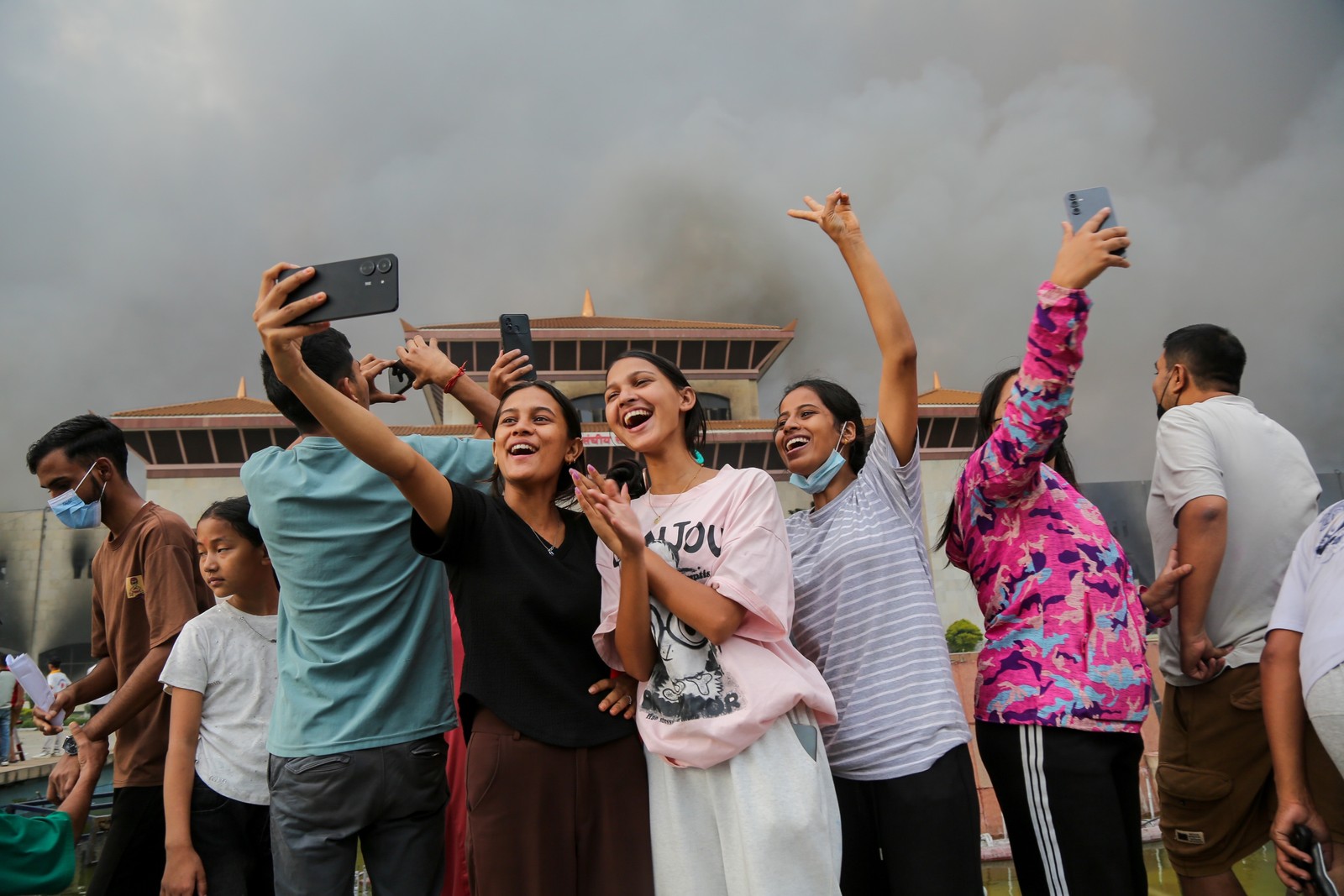 Demonstrators smile and take selfies, standing in front of a smoldering building.
