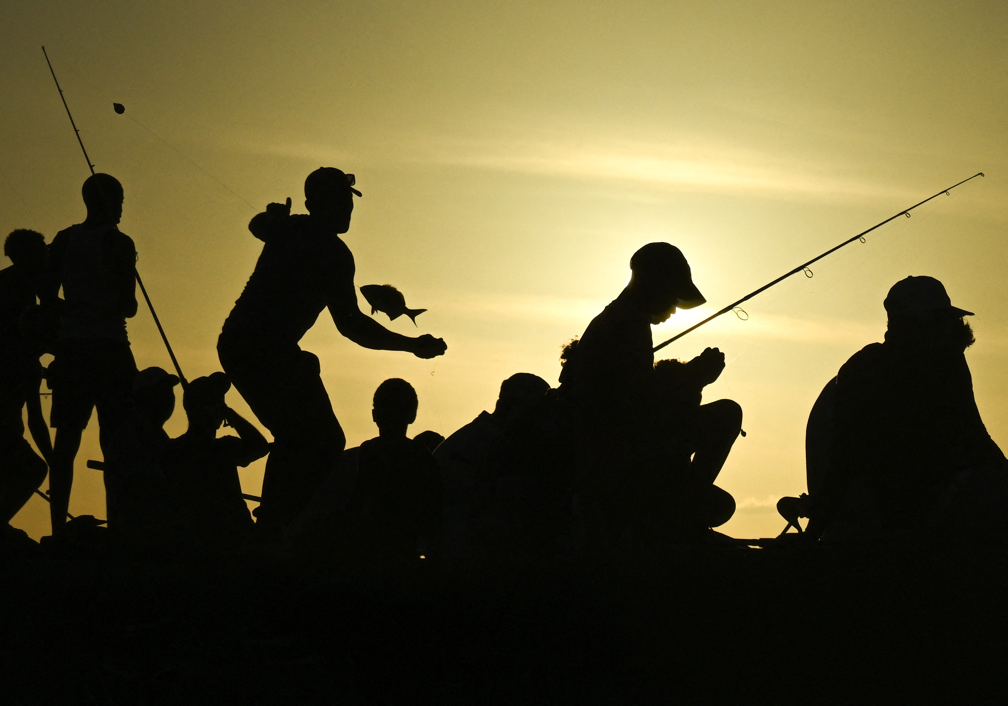 People fish at sunset, seen in silhouettte.