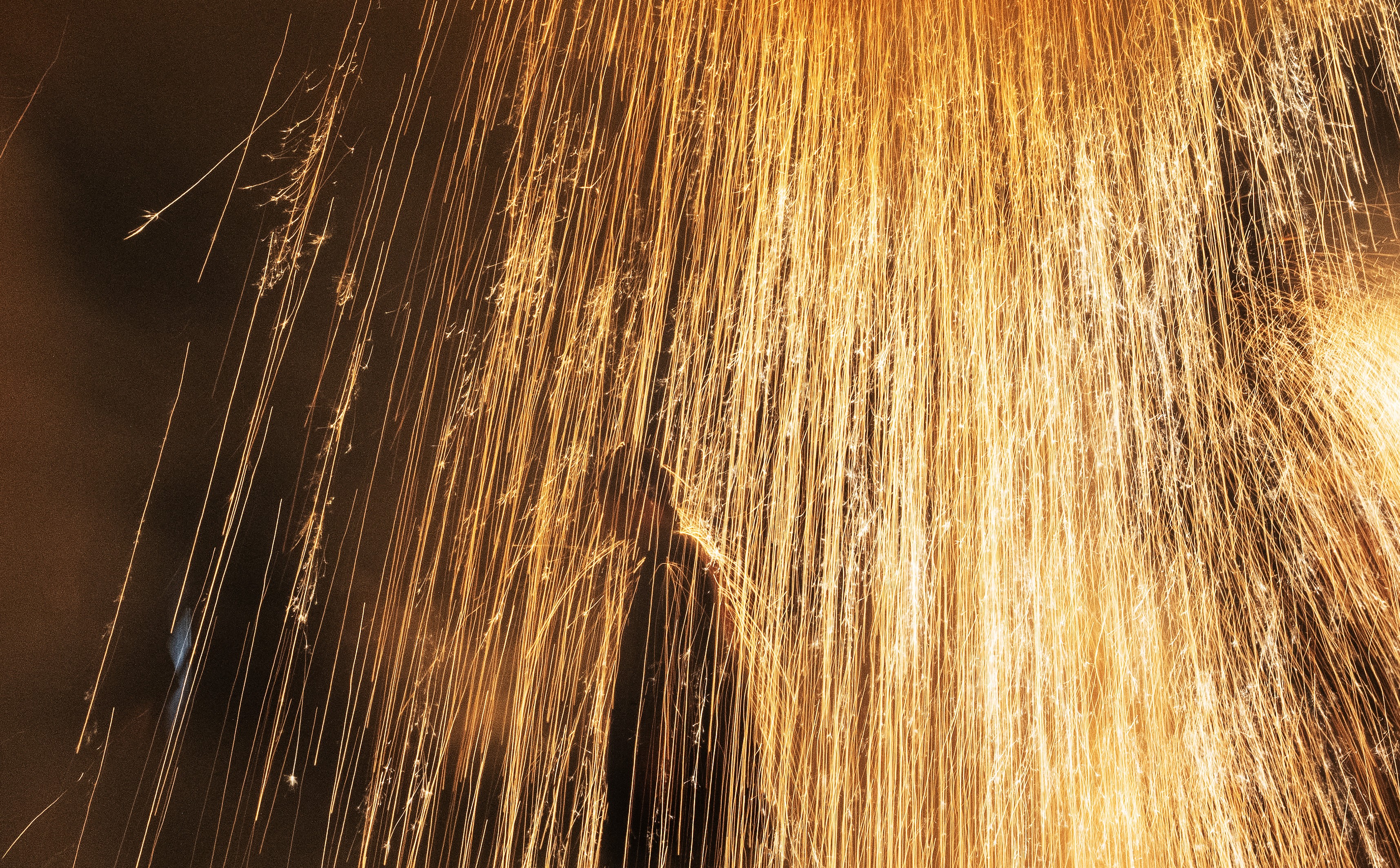 A performer stands under a huge shower of sparks, with some bouncing off their head and shoulders.