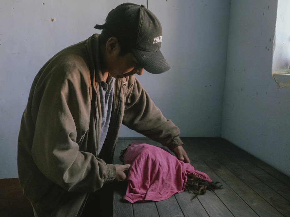 A man uses a pink cloth to carefully wrap the khipus on a wooden table in a blue room at the museum in Jucul.