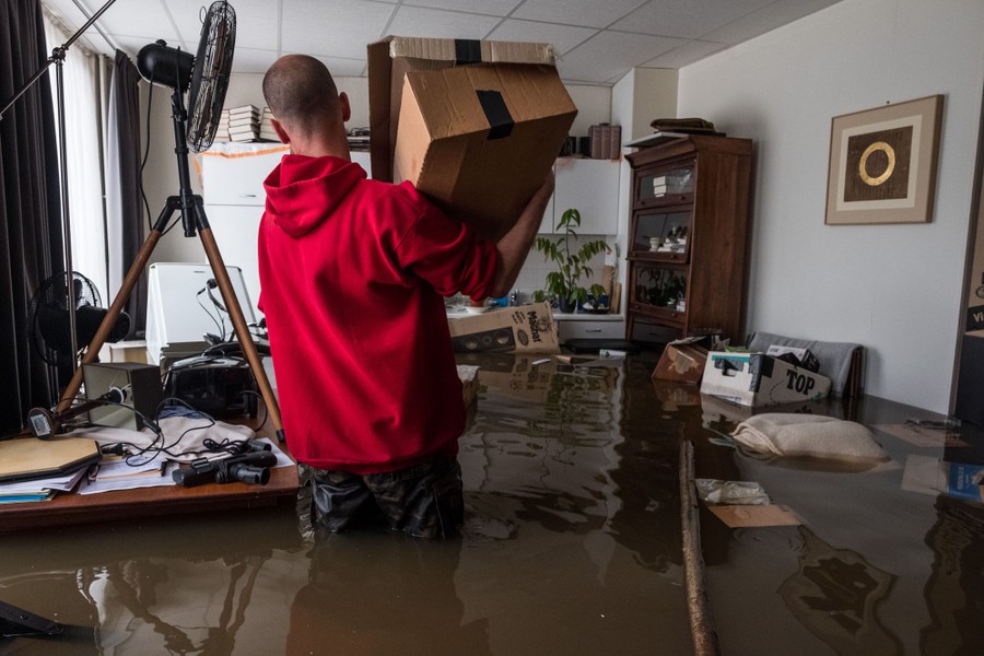 A man holds a box inside a flooded house.