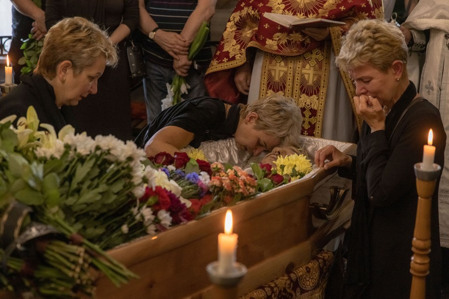 People stand and kneel around an open coffin during a funeral service.