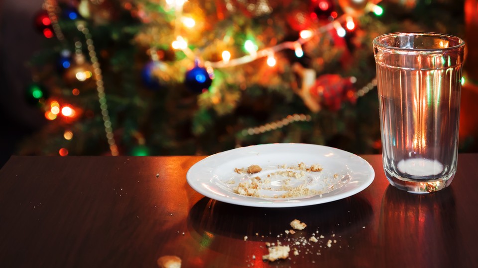 An empty glass of milk and a plate of cookie crumbs sit in front of a Christmas tree