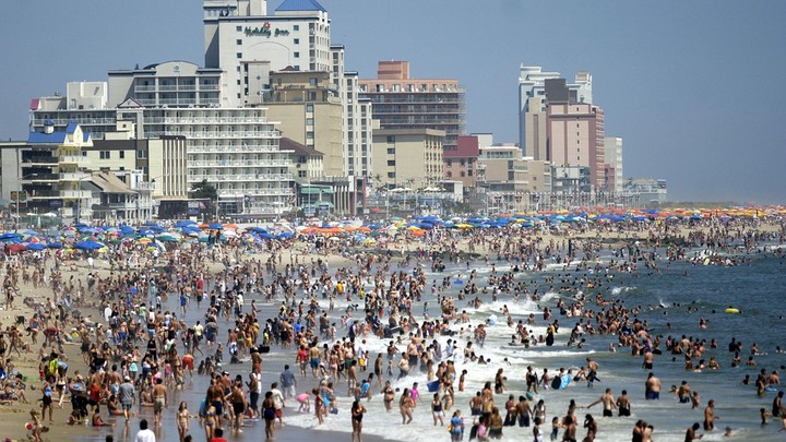 People and beach umbrellas pack the shores of Ocean City, Maryland. Hotels and other buildings also dot the coastline.