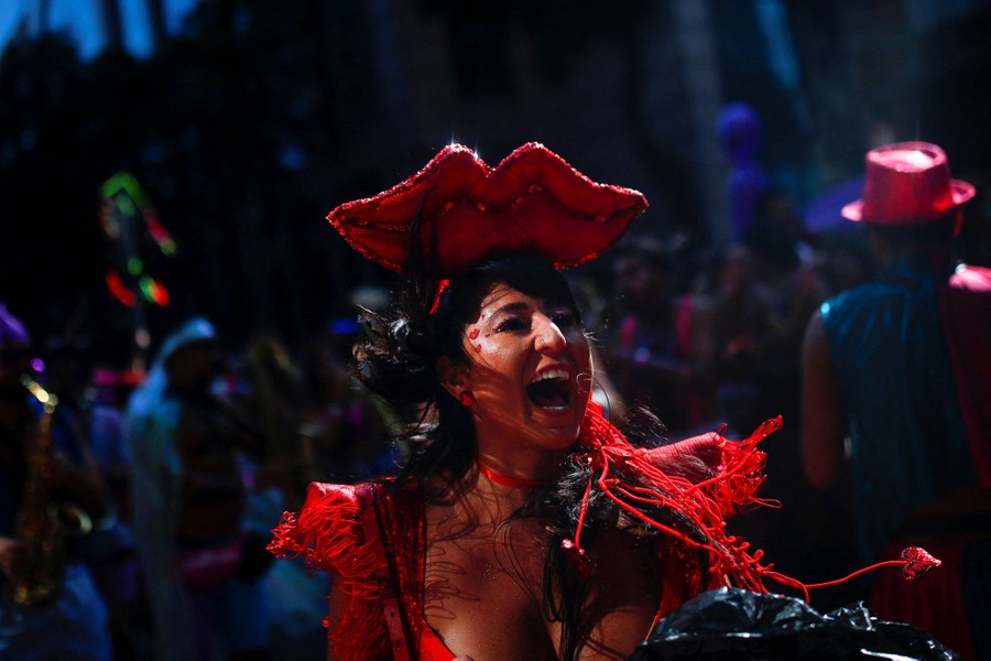 A costumed person wearing a large pair of red lips on top of their head celebrates among others.