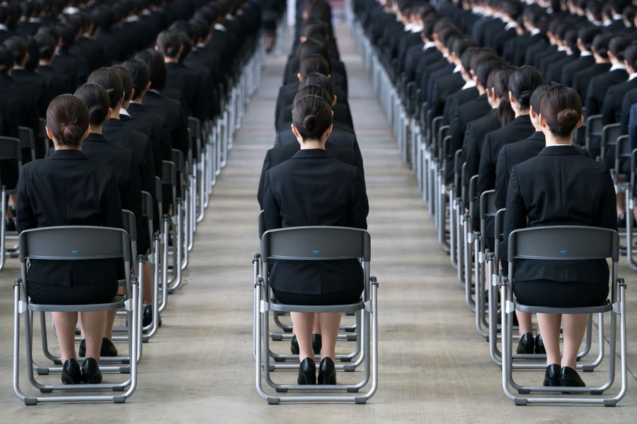 Dozens of uniformed people sit in folding chairs arranged in neat rows.