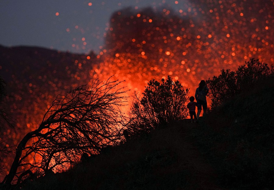 A woman and child are seen on a hillside, silhouetted against lava from an eruption.