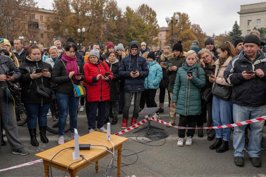 A crowd of people gather around an access point to the internet, set up outside on a small table on pavement.