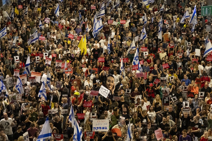 Demonstrators in Israel hold up signs and Israeli flags during a march.