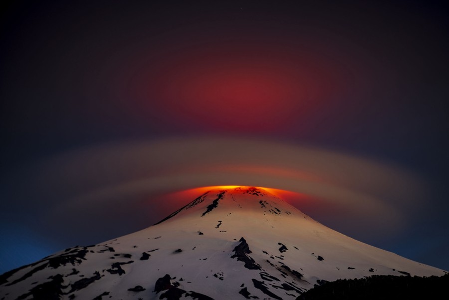 Low clouds cover the tip of a volcano, illuminated by the glowing lava below.