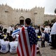 A man wearing an American flag in front of students waving Israeli flags