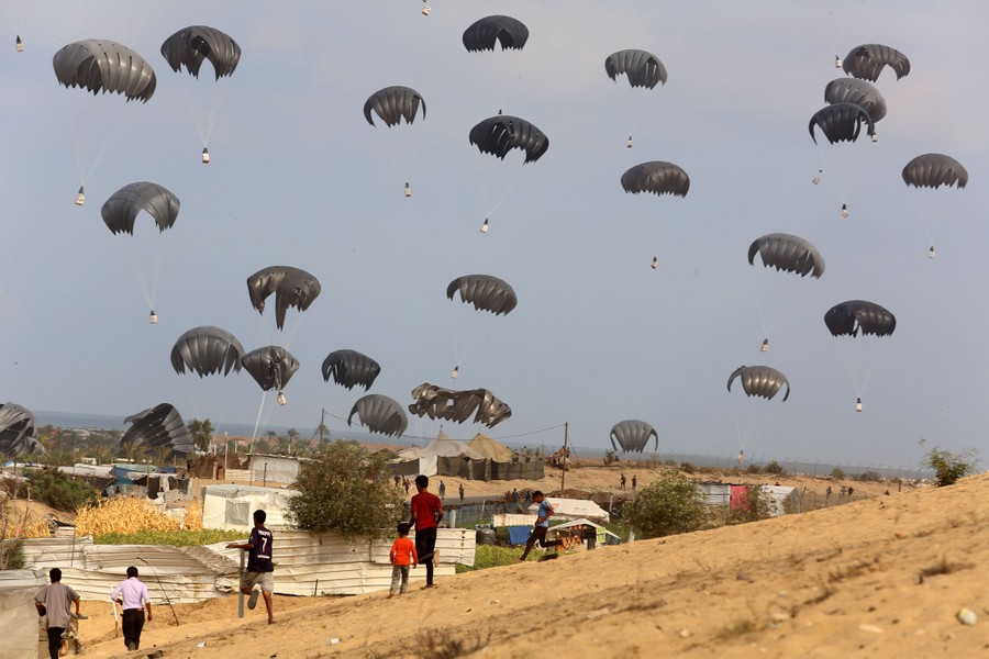 People watch as a couple dozen parachutes fall to the ground, each carrying crates.