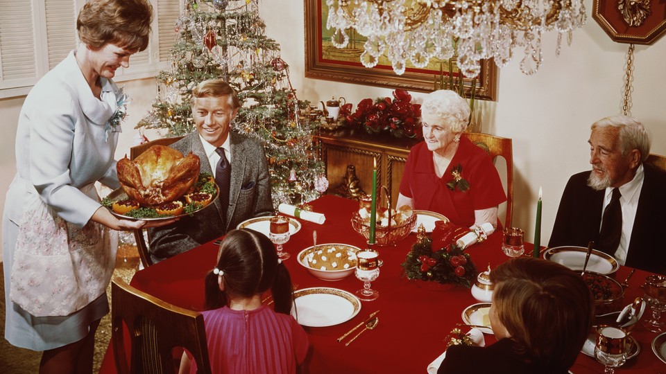 A mother bringing a large turkey to the table for Christmas dinner, circa 1965