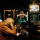 An old man holds his head watching the TV at a bar alone