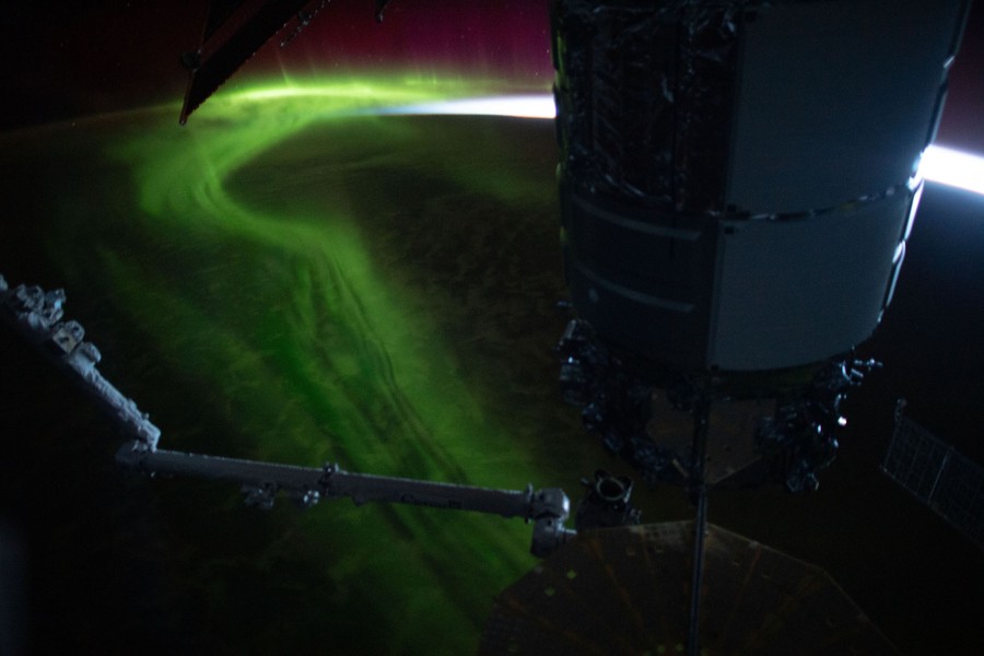 Greenish bands of light swirl above the Earth at night, seen from orbit.