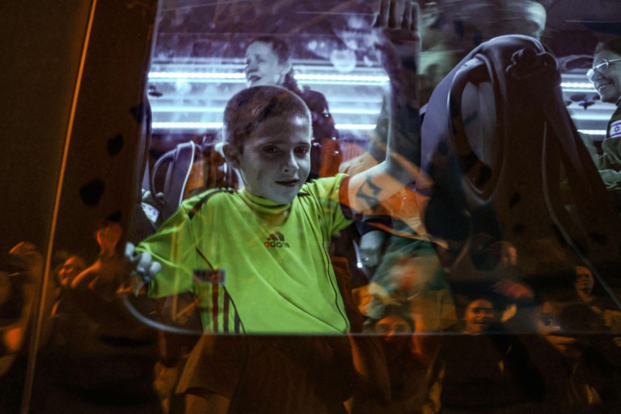 A boy stands inside a bus, waving and looking out.