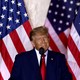 A photograph of Donald Trump at a podium in front of three American flags